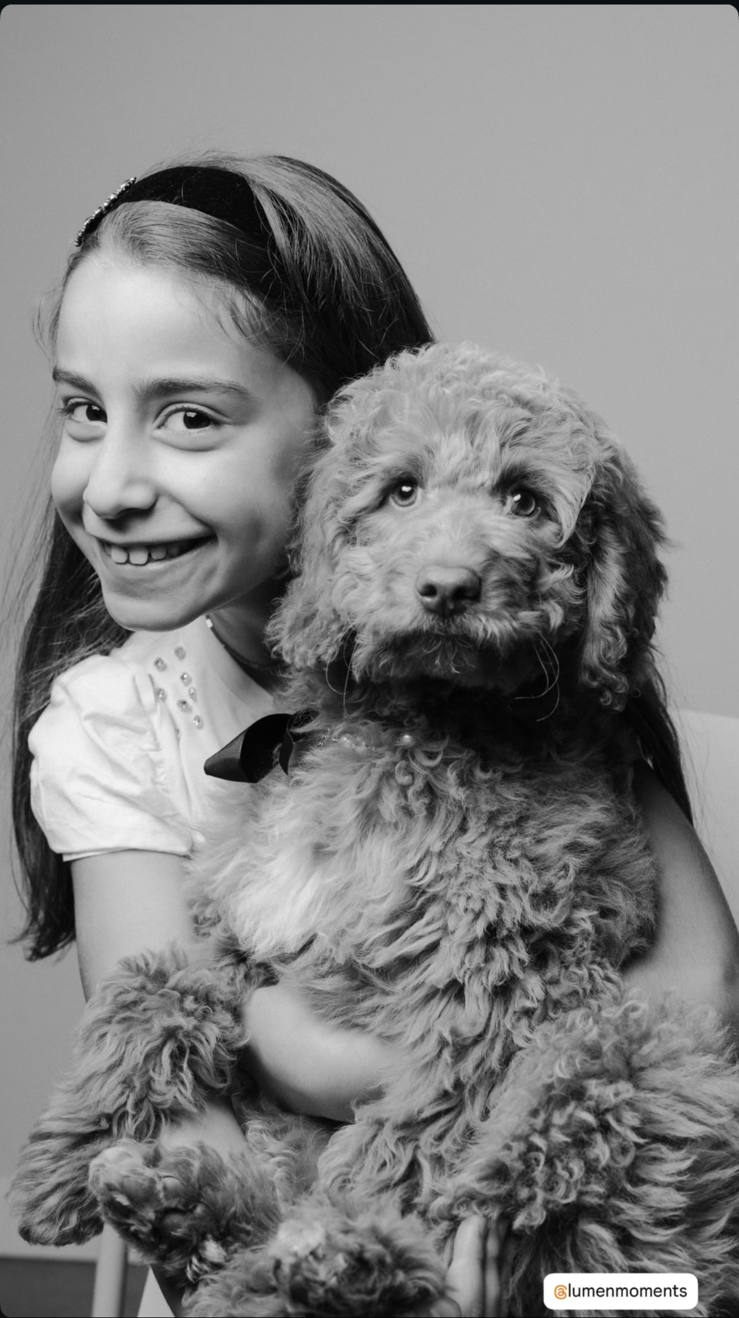 A young Kid's Best Doodle family member with her Goldendoodle puppy — portrait by Lumen Moments