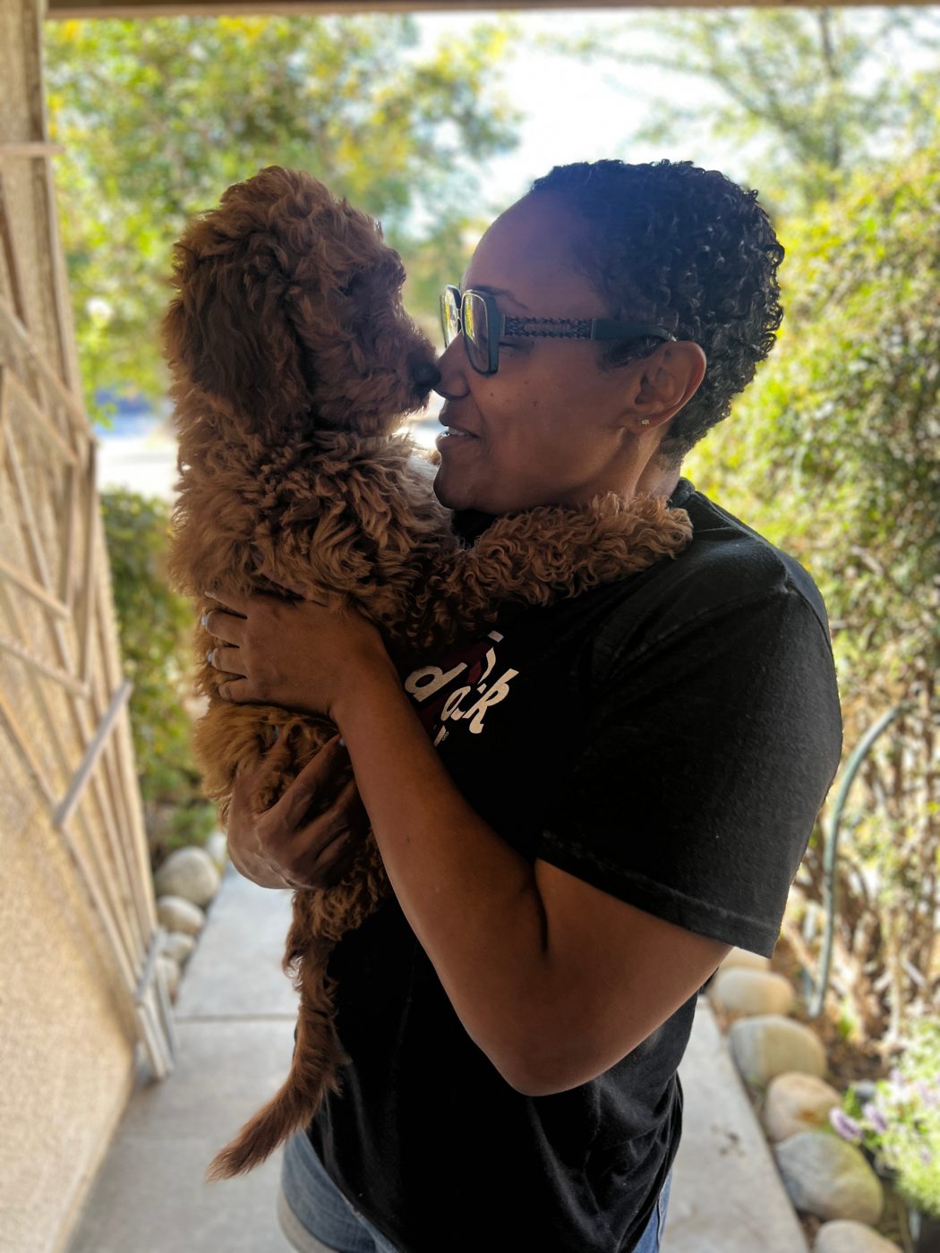 Owner holding her red Goldendoodle puppy nose-to-nose at the front door during the puppy's first days home