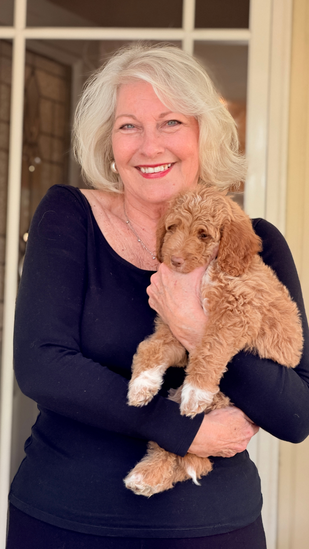 A grandmother on her doorway holding her new Kid's Best Doodle Goldendoodle puppy on homecoming day