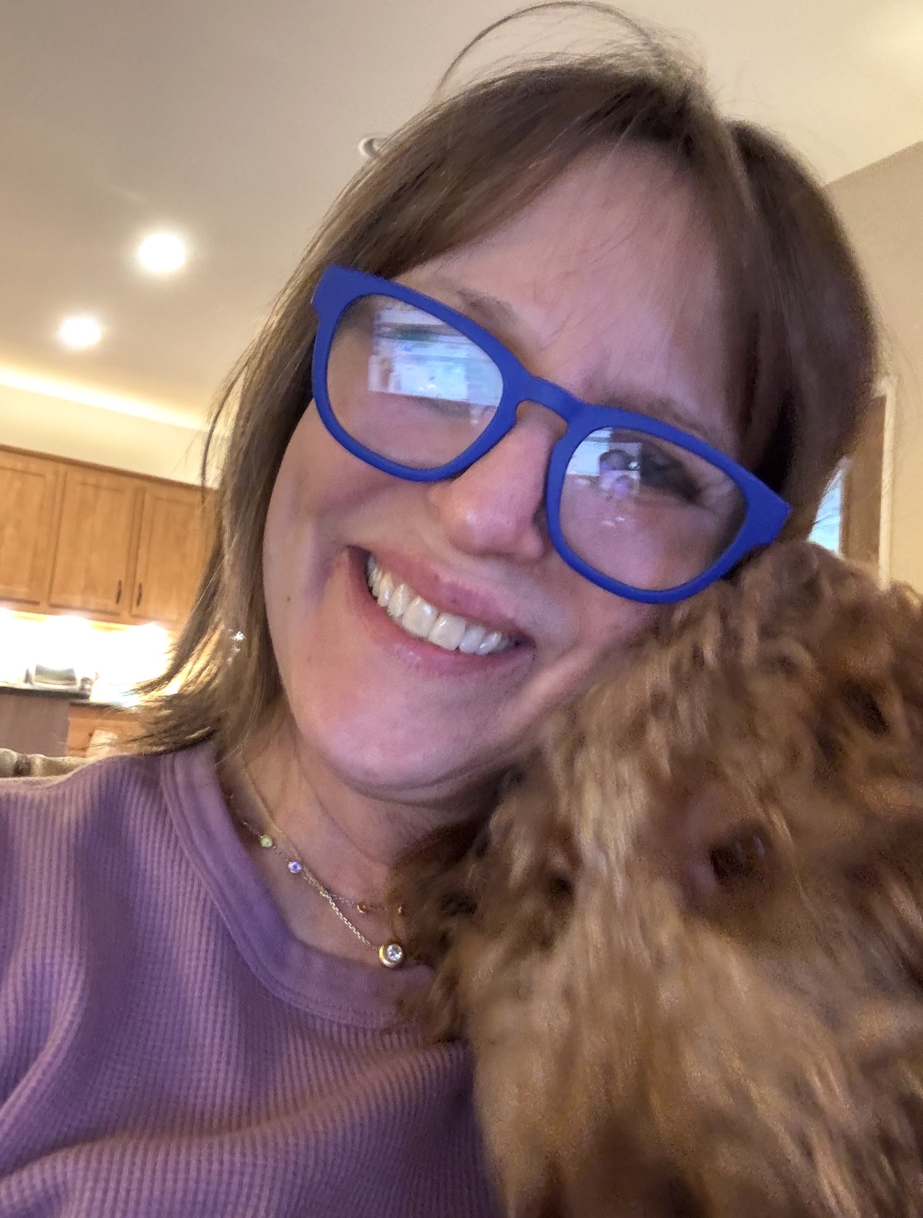 A Kid's Best Doodle mom smiling as her red Goldendoodle puppy nuzzles into her cheek