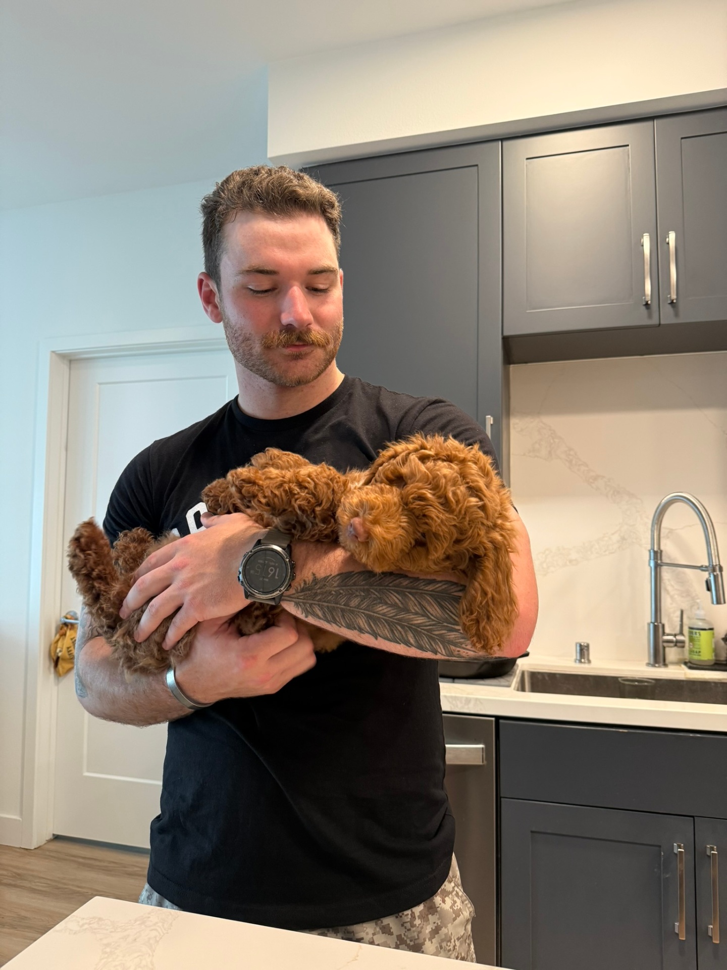 A young Kid's Best Doodle owner cradling his sleeping red Goldendoodle puppy in his kitchen on homecoming day