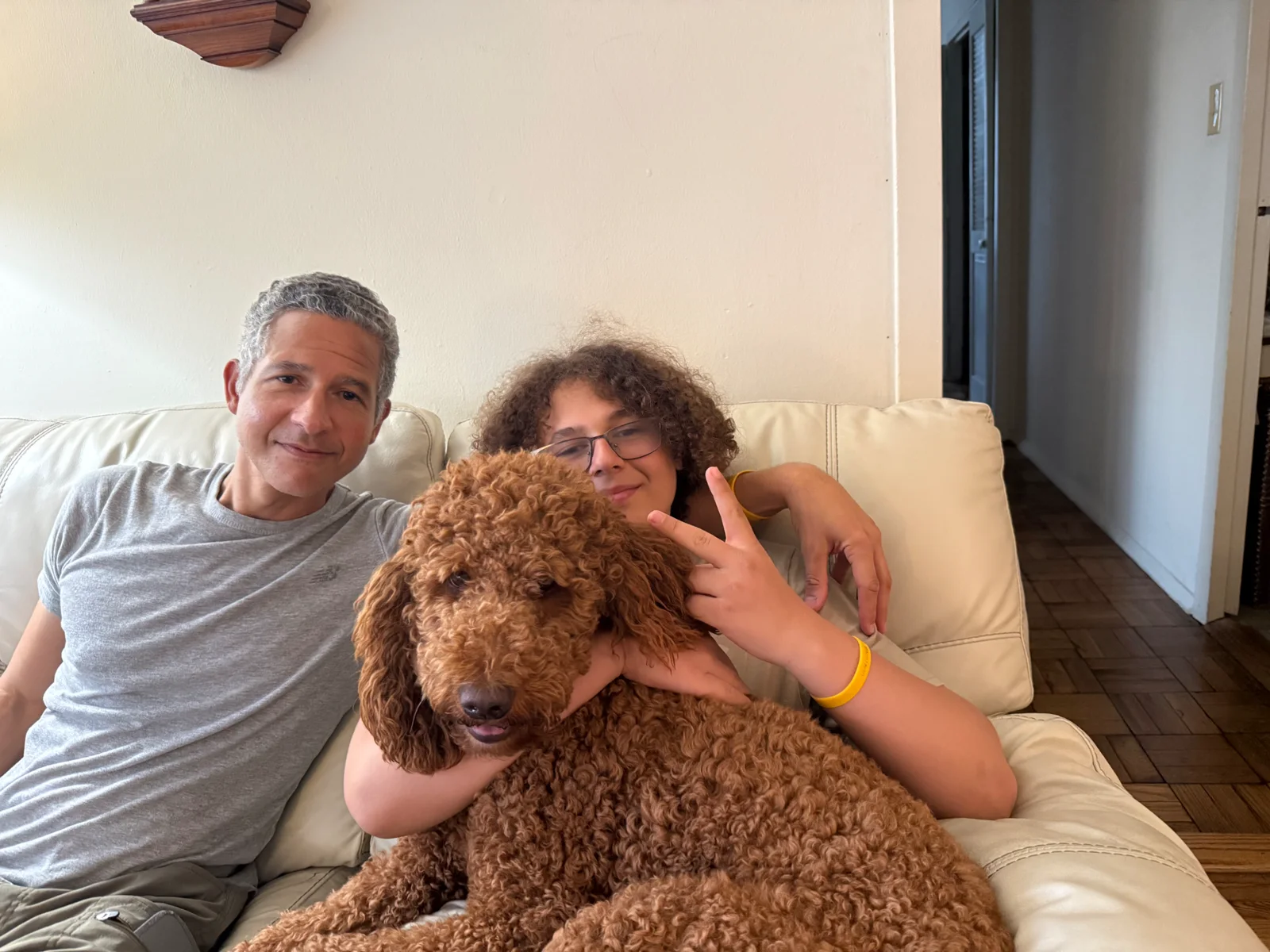 A family settled on the couch at home in the evening with their red Goldendoodle